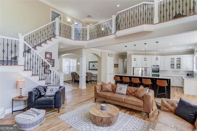 living room with ornate columns, crown molding, a high ceiling, and light wood-type flooring