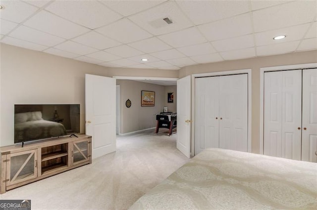 carpeted bedroom featuring two closets and a drop ceiling