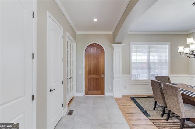 entryway with ornate columns, crown molding, a chandelier, and light wood-type flooring