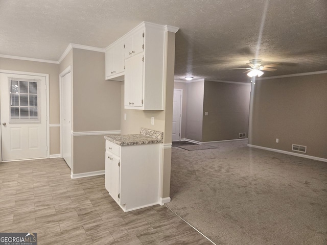 kitchen featuring light stone countertops, light colored carpet, white cabinetry, and crown molding