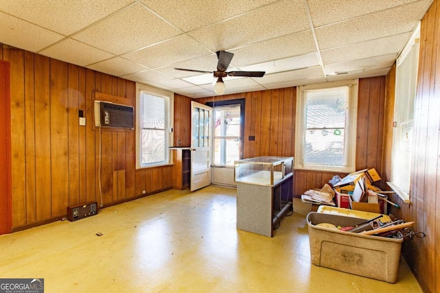 interior space with ceiling fan, a drop ceiling, and wood walls