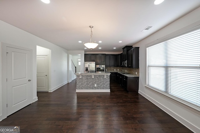 kitchen with hanging light fixtures, stainless steel appliances, tasteful backsplash, dark hardwood / wood-style flooring, and a kitchen island