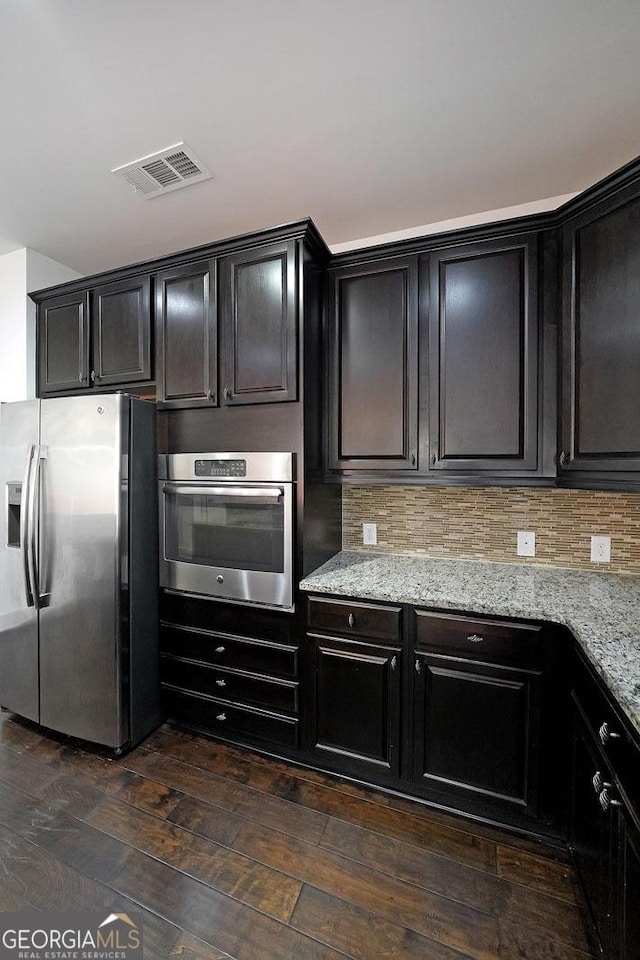 kitchen with light stone countertops, dark hardwood / wood-style flooring, stainless steel appliances, and backsplash