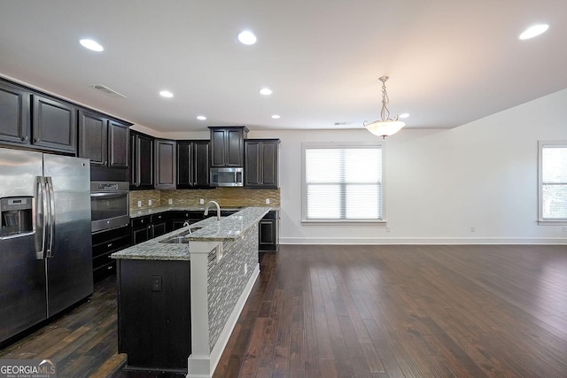 kitchen with sink, light stone counters, backsplash, a center island with sink, and appliances with stainless steel finishes