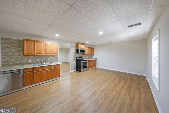 kitchen featuring a drop ceiling, backsplash, sink, light wood-type flooring, and appliances with stainless steel finishes