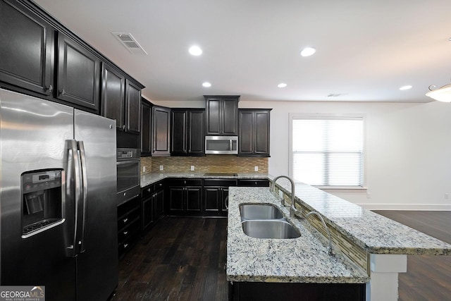 kitchen with a kitchen island with sink, sink, light stone counters, and appliances with stainless steel finishes