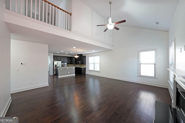 unfurnished living room with ceiling fan, a towering ceiling, and dark wood-type flooring