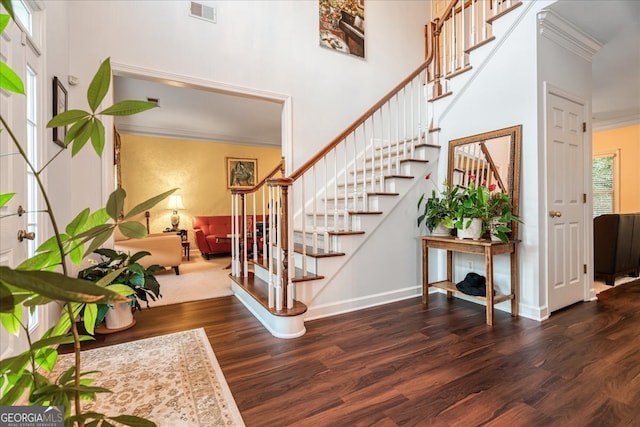 foyer entrance featuring a towering ceiling, dark hardwood / wood-style floors, and ornamental molding