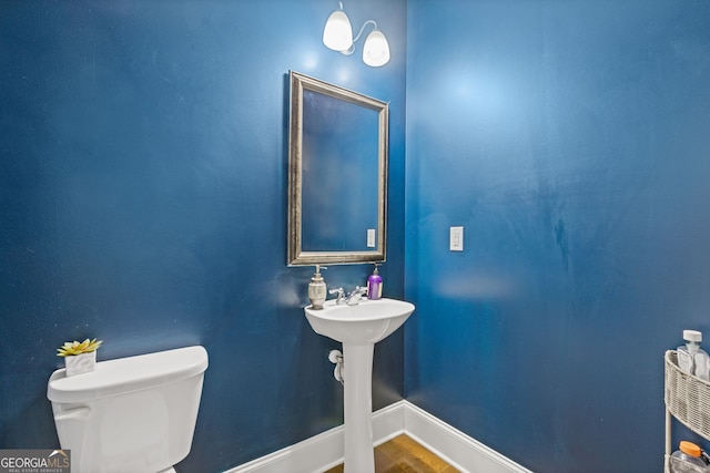 half bath with wood finished floors, toilet, and baseboards