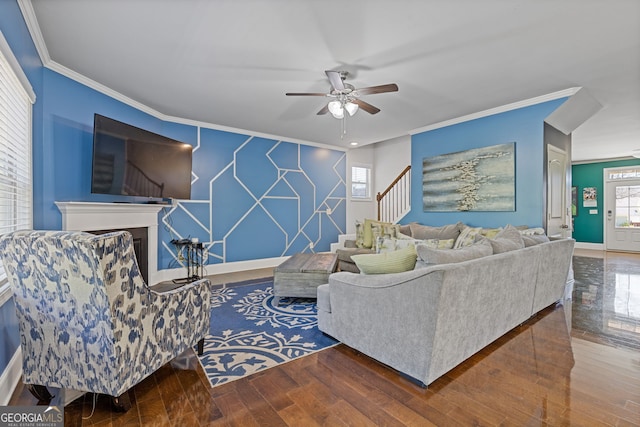 living area featuring a fireplace, an accent wall, ornamental molding, wood finished floors, and baseboards