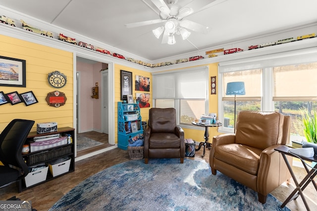 living area with ceiling fan and wood walls