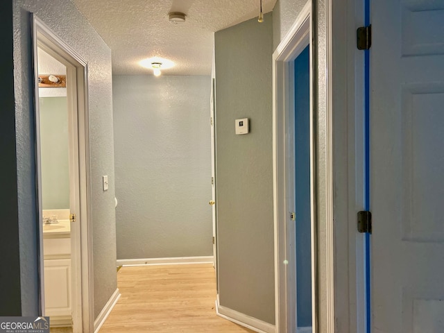 corridor featuring sink, a textured ceiling, and light hardwood / wood-style flooring