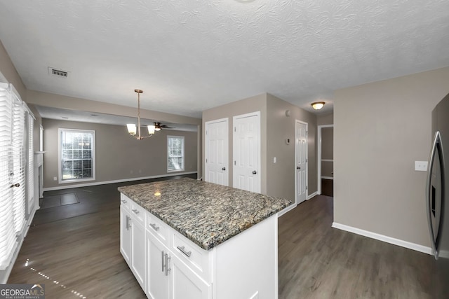 kitchen with hanging light fixtures, dark hardwood / wood-style floors, dark stone countertops, a kitchen island, and white cabinetry