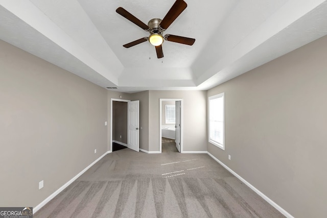 unfurnished bedroom with ceiling fan, light carpet, and a tray ceiling