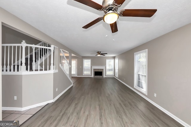 unfurnished living room with a tiled fireplace, ceiling fan, a textured ceiling, and hardwood / wood-style flooring