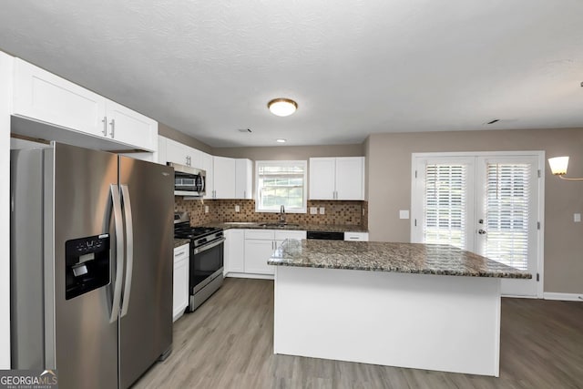 kitchen featuring light wood-type flooring, dark stone counters, stainless steel appliances, a kitchen island, and white cabinetry