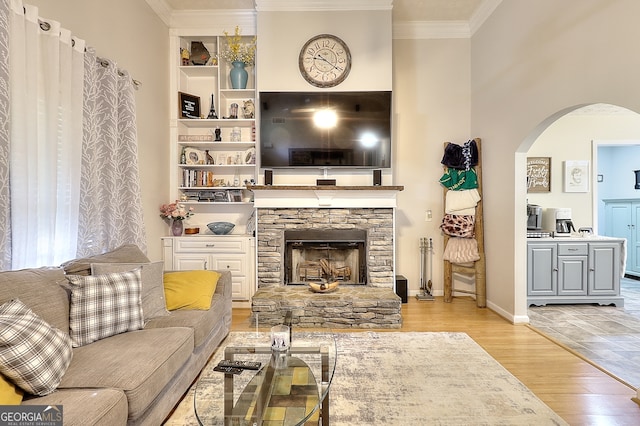 living room featuring a stone fireplace, crown molding, and light hardwood / wood-style flooring