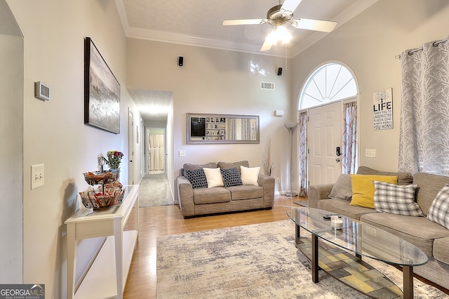 living room featuring a high ceiling, light hardwood / wood-style floors, ceiling fan, and crown molding