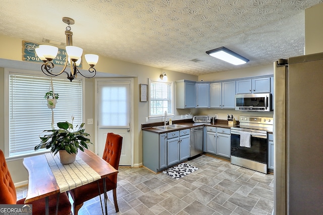 kitchen featuring appliances with stainless steel finishes, a textured ceiling, sink, decorative light fixtures, and a notable chandelier