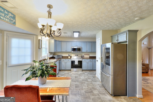 kitchen featuring sink, a chandelier, pendant lighting, a textured ceiling, and appliances with stainless steel finishes