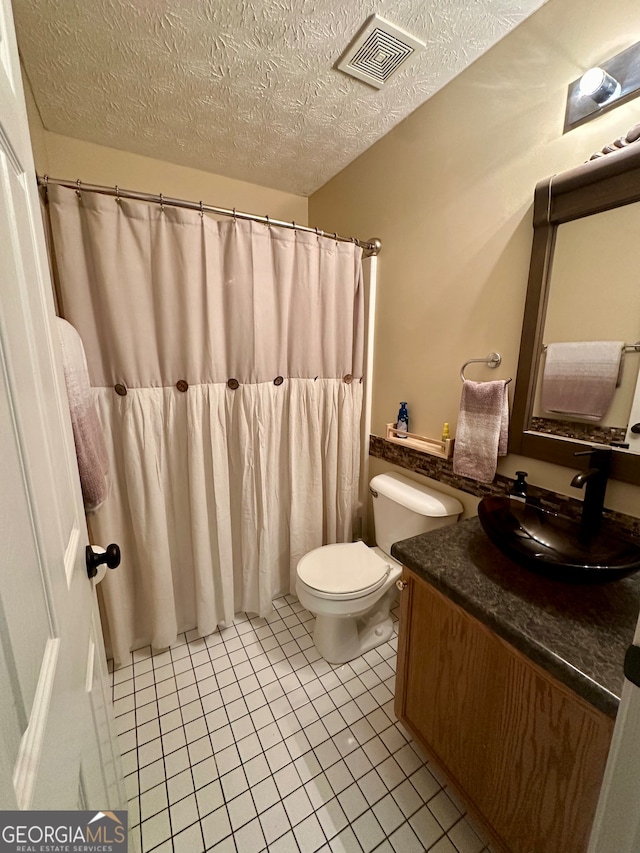 bathroom with tile patterned flooring, vanity, a textured ceiling, and toilet