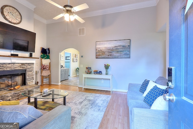 living room featuring ceiling fan, ornamental molding, a fireplace, a towering ceiling, and light hardwood / wood-style floors