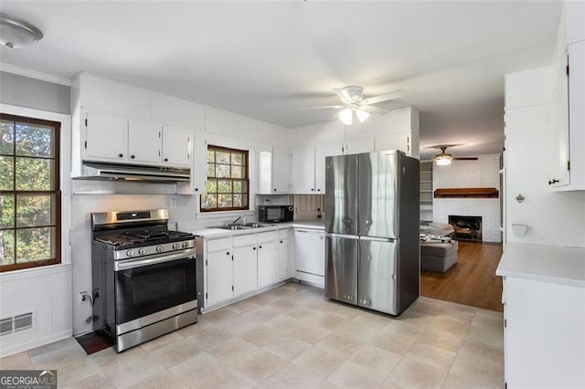 kitchen with appliances with stainless steel finishes, a brick fireplace, ceiling fan, sink, and white cabinets