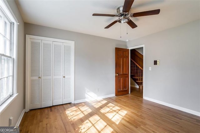 unfurnished bedroom featuring ceiling fan, a closet, light hardwood / wood-style flooring, and multiple windows