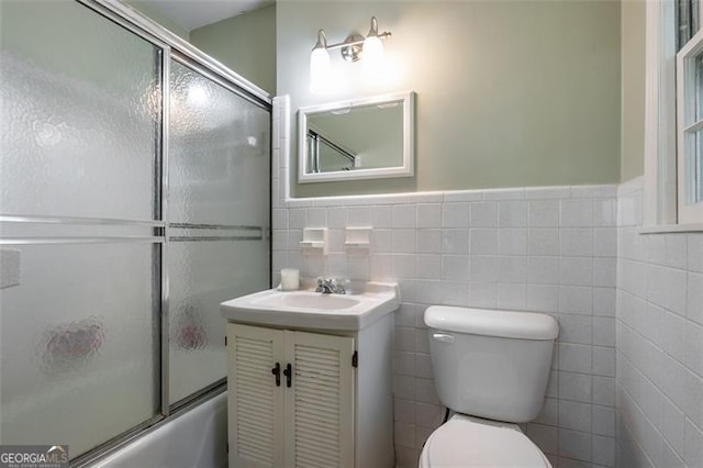 full bathroom with combined bath / shower with glass door, vanity, toilet, and tile walls