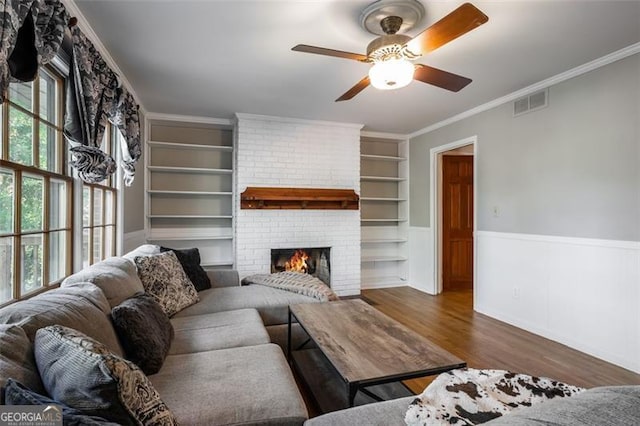 living room featuring crown molding, ceiling fan, built in features, a fireplace, and dark hardwood / wood-style flooring