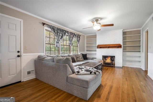 living room with built in shelves, ceiling fan, crown molding, hardwood / wood-style floors, and a fireplace