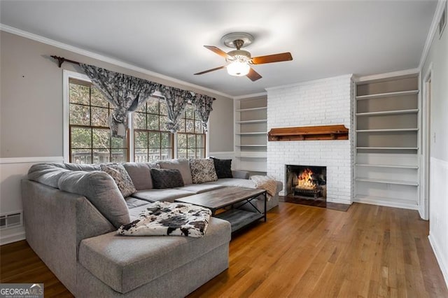 living room featuring ceiling fan, crown molding, hardwood / wood-style flooring, built in features, and a fireplace