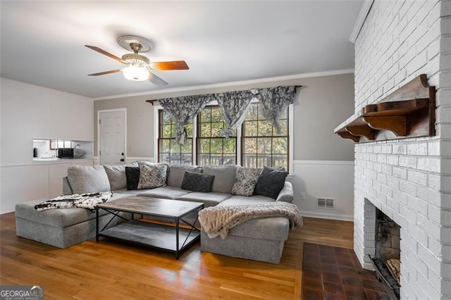 living room featuring wood-type flooring, a brick fireplace, ceiling fan, and crown molding