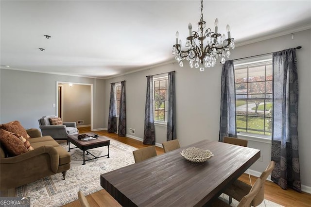 dining space with plenty of natural light, an inviting chandelier, ornamental molding, and light hardwood / wood-style flooring