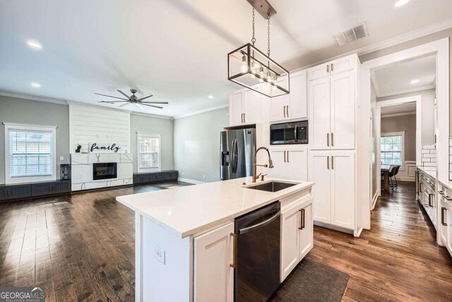 kitchen featuring stainless steel appliances, sink, white cabinets, hanging light fixtures, and an island with sink