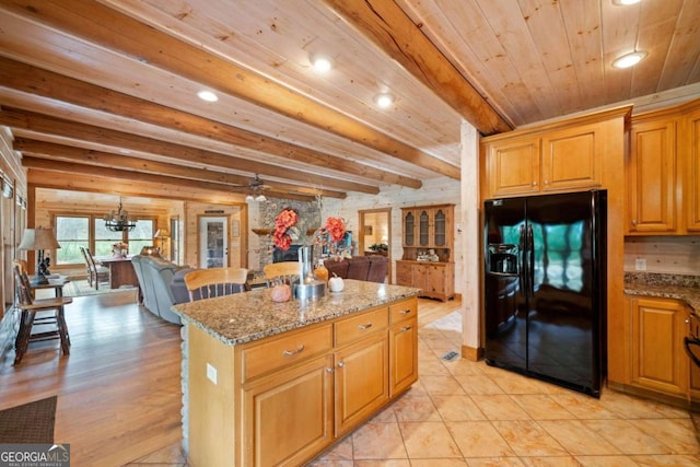 kitchen featuring light wood-type flooring, black refrigerator with ice dispenser, light stone counters, beamed ceiling, and a center island