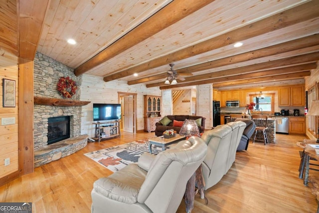 living room with ceiling fan, a stone fireplace, light hardwood / wood-style flooring, beamed ceiling, and wood walls