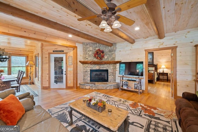 living room with a stone fireplace, wooden walls, hardwood / wood-style flooring, ceiling fan, and beam ceiling