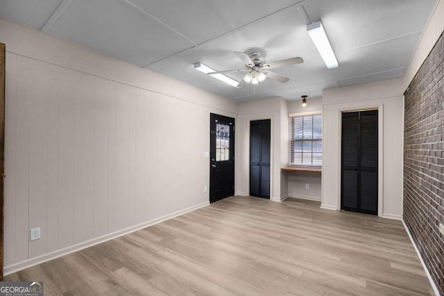 empty room with wooden walls, ceiling fan, light wood-type flooring, and brick wall