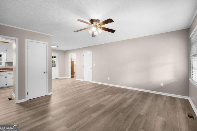 unfurnished living room featuring ceiling fan, wood-type flooring, a textured ceiling, and ornamental molding