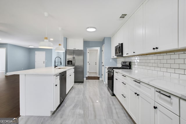 kitchen with a kitchen island with sink, white cabinets, sink, decorative light fixtures, and stainless steel appliances