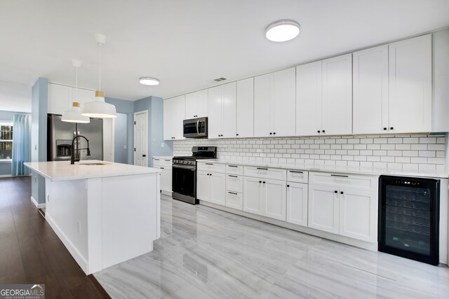 kitchen featuring white cabinets, hanging light fixtures, stainless steel appliances, and beverage cooler