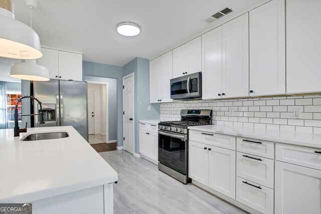 kitchen with appliances with stainless steel finishes, backsplash, sink, decorative light fixtures, and white cabinets