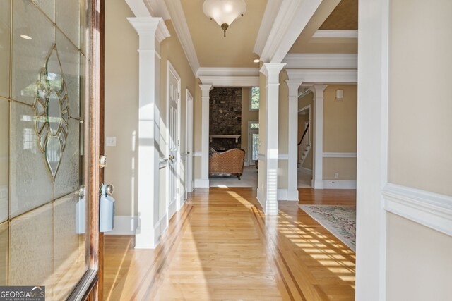 entrance foyer featuring hardwood / wood-style floors, decorative columns, a stone fireplace, and ornamental molding