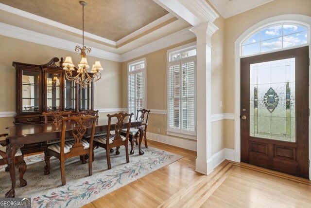 dining space featuring an inviting chandelier, decorative columns, light hardwood / wood-style floors, a tray ceiling, and ornamental molding