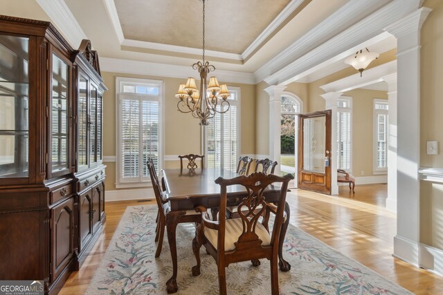 dining space featuring a raised ceiling, light hardwood / wood-style flooring, ornate columns, and a healthy amount of sunlight