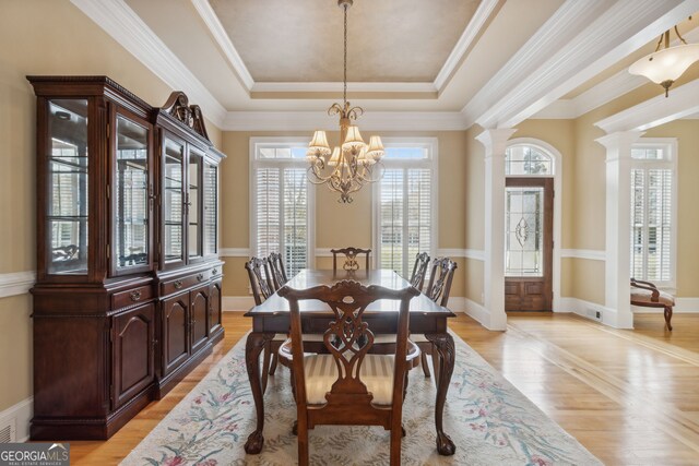 dining area featuring an inviting chandelier, light wood-type flooring, ornamental molding, a tray ceiling, and decorative columns