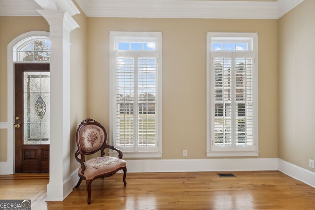 living area featuring decorative columns, light hardwood / wood-style flooring, and ornamental molding