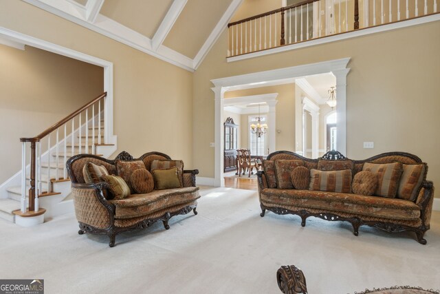 carpeted living room featuring ornate columns, crown molding, high vaulted ceiling, and an inviting chandelier