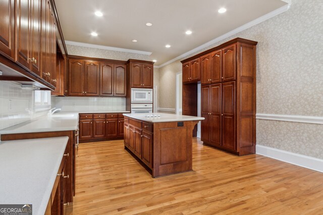 kitchen featuring light wood-type flooring, white appliances, a center island, and ornamental molding